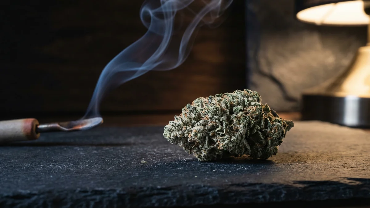 Cannabis bud with crystalline trichome structures and a wisp of smoke suggesting decarboxylation